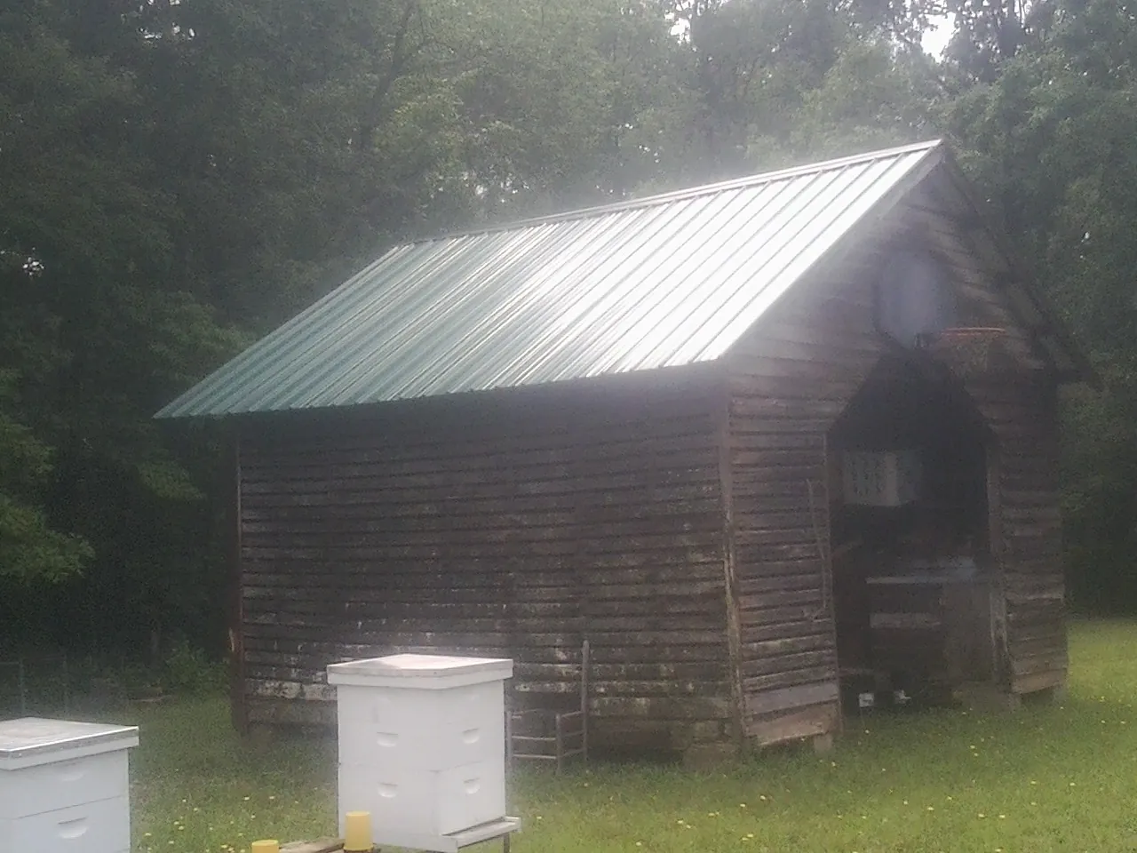 Green metal roof on a weathered barn beside stacked beehives in Bennington