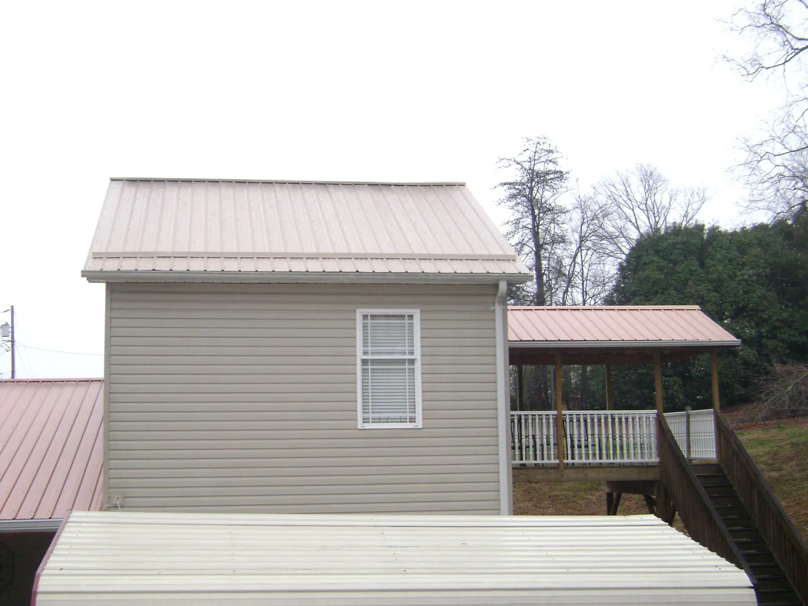 Tan metal roofs on a two story addition and attached porch, from a Roof Replacement job in Bennington